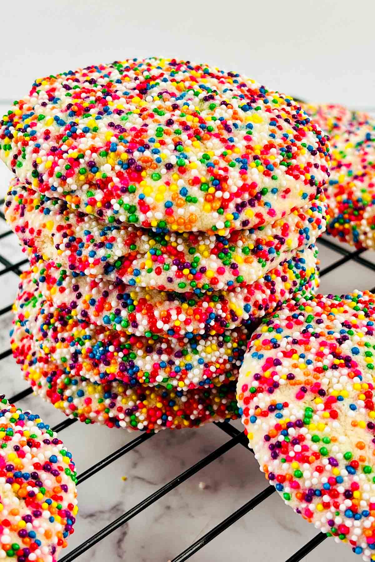 Side view of sprinkle cookies stacked on a cooling rack.