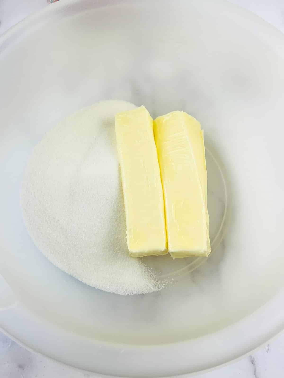 Sticks of butter and granulated sugar in a mixing bowl.