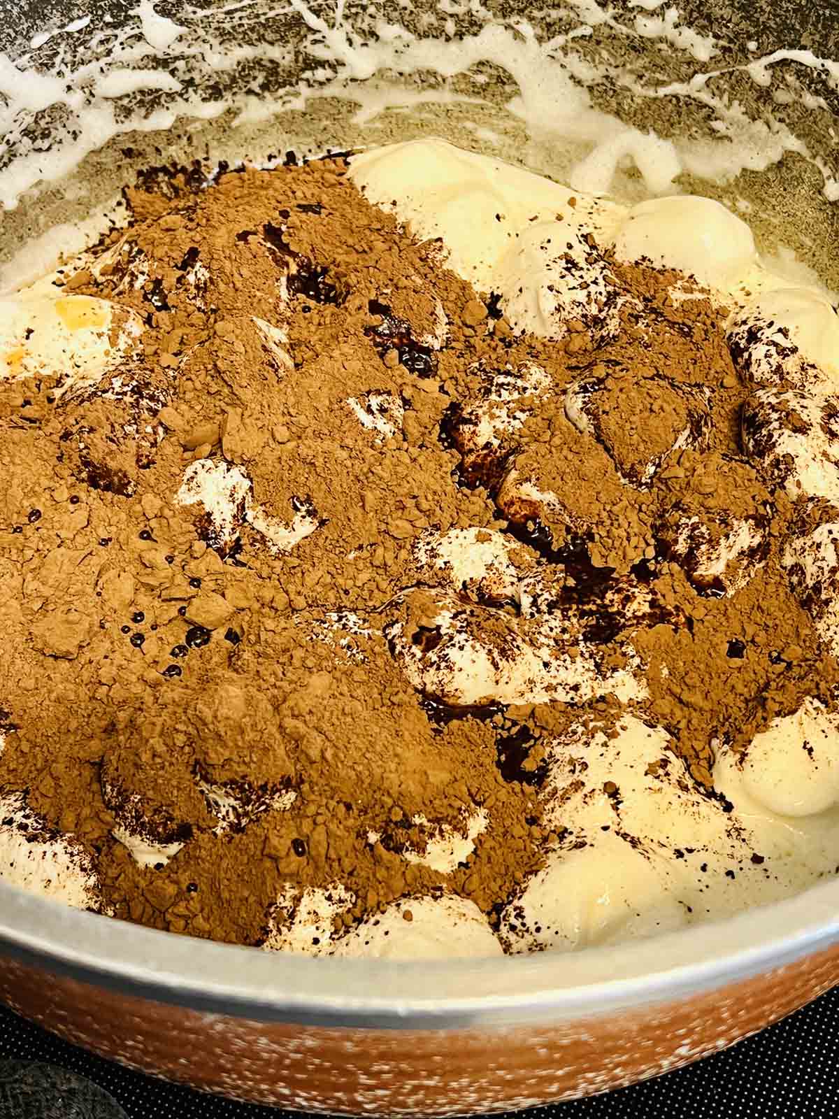 Cocoa powder over marshmallows in a pot.