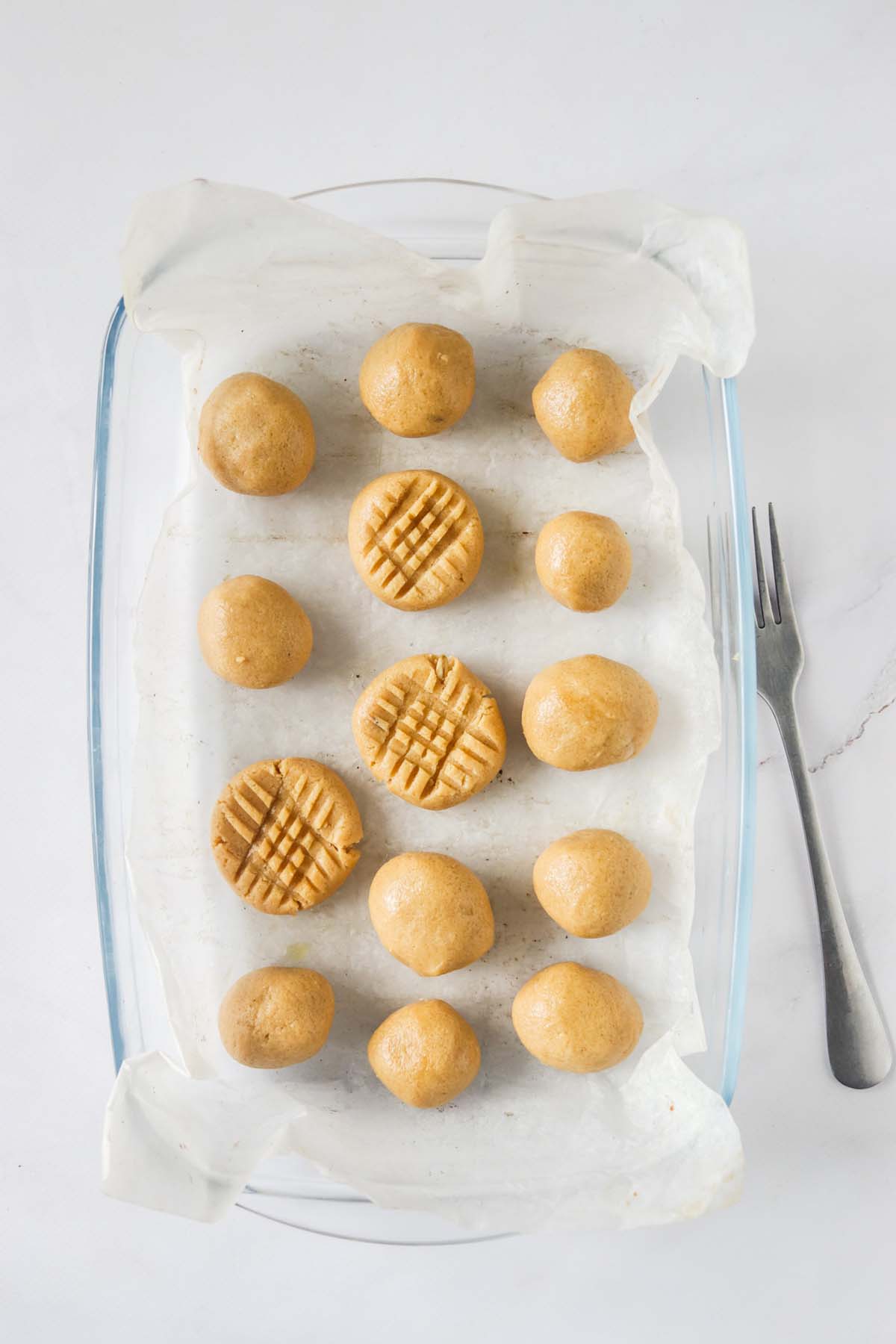 Balls of cookie dough on parchment paper with criss cross pattern on a few.