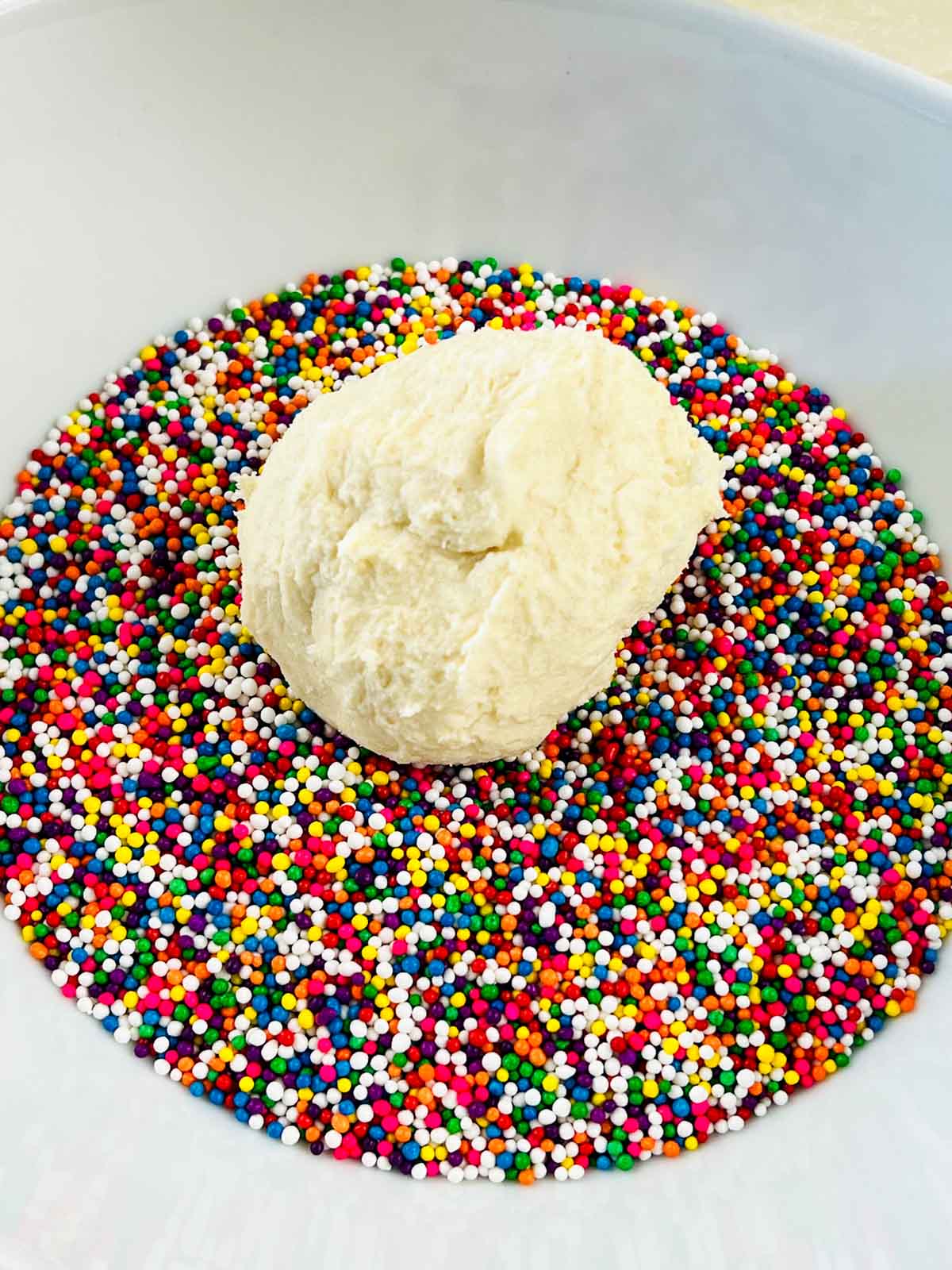 A ball of cookie dough in a bowl with sprinkles.