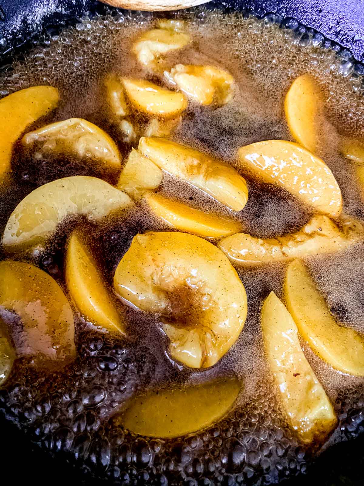 Peaches simmering in the syrup in the skillet.