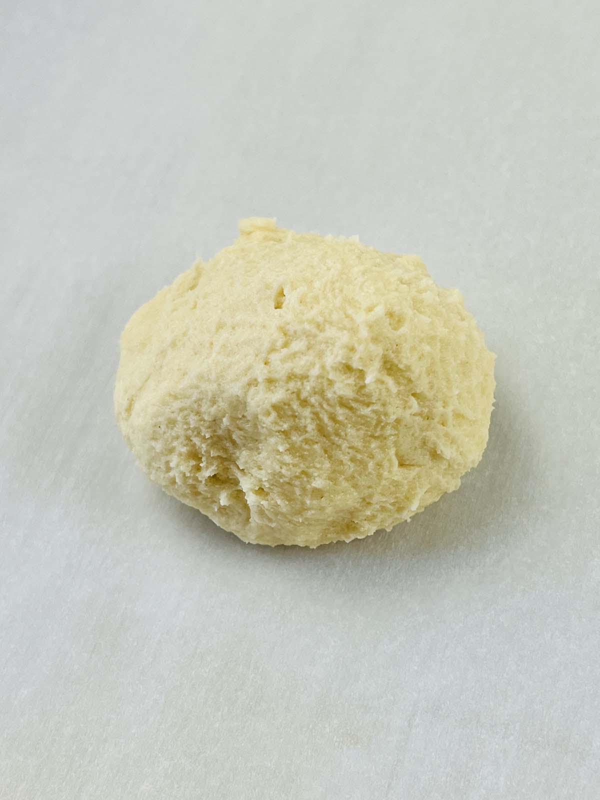 A rounded drop of cookie dough on parchment paper.