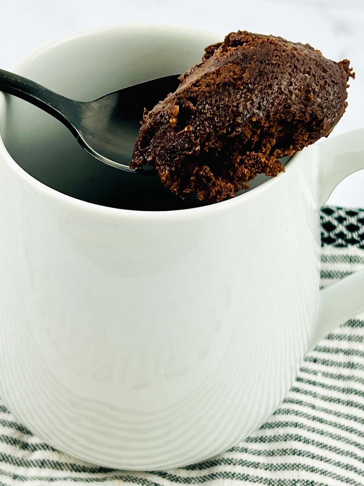 A scoop of cake on a spoon resting on a mug.