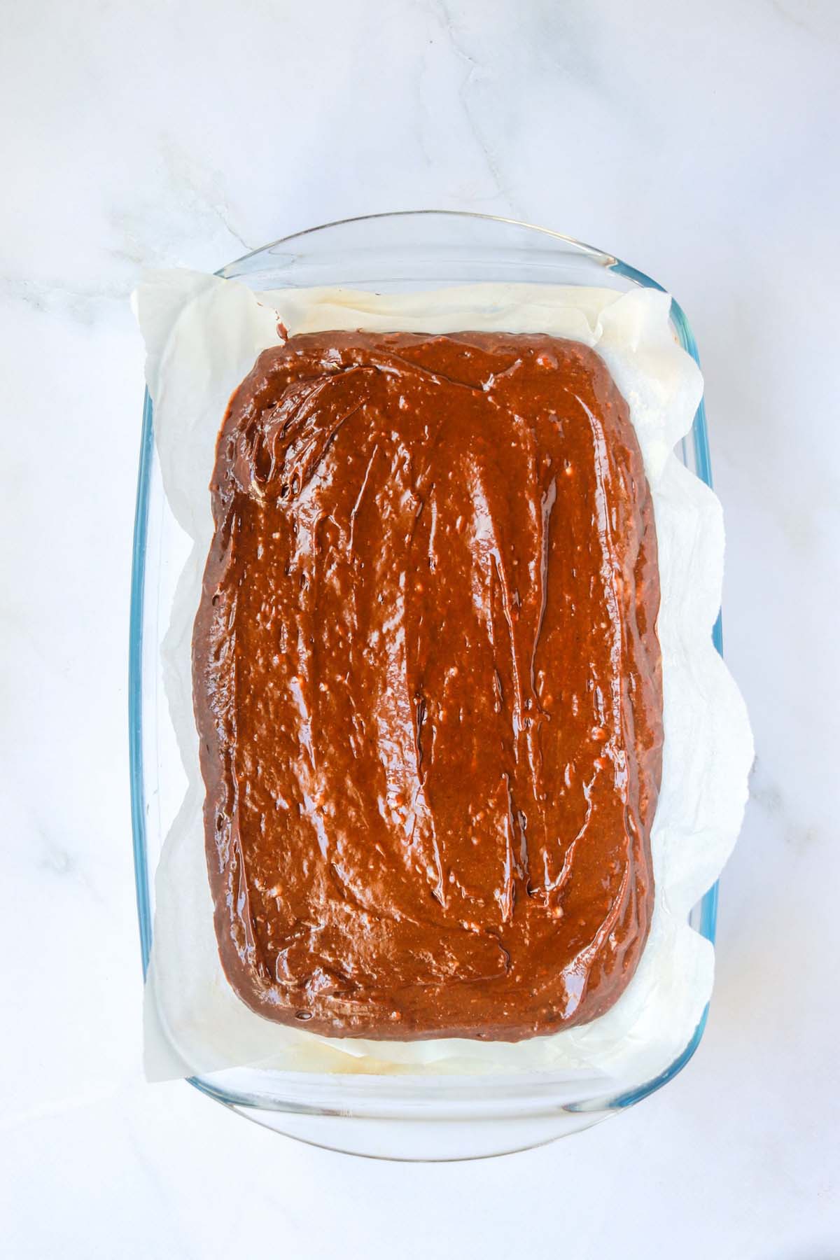 Brownie batter spread out in a baking dish lined with parchment paper.
