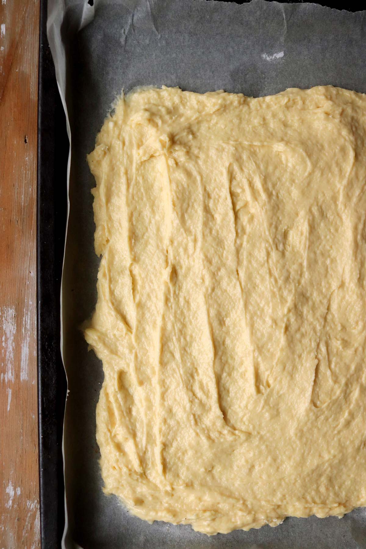 Sugar cookie dough spread in a baking sheet lined with parchment paper.