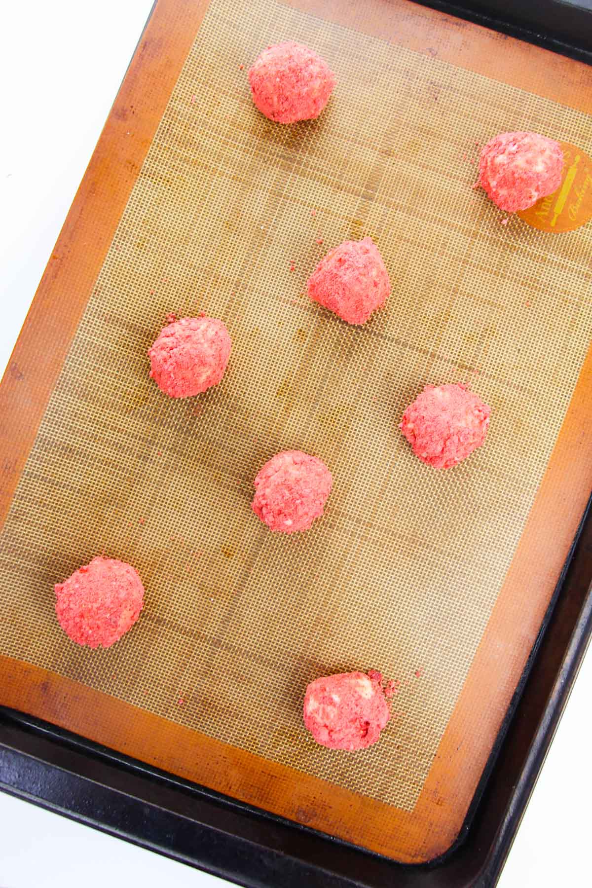 Cookie dough balls on a baking sheet lined with a silicone mat.