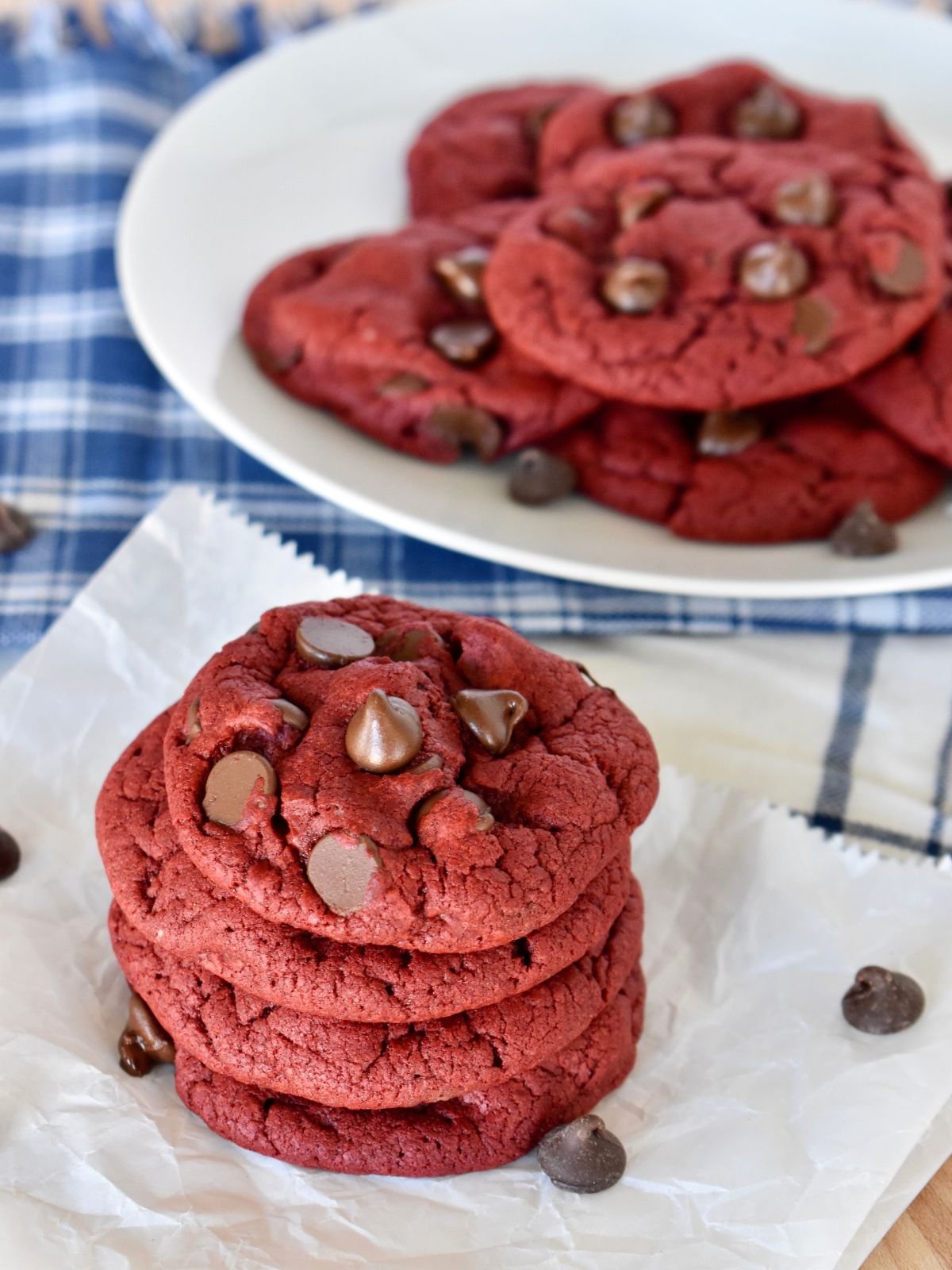 Red Velvet Cake Mix Cookies on a piece of parchment paper with more cookies on a plate behind it. 