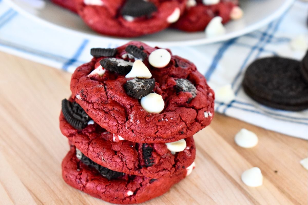 Red Velvet Oreo Cookies stacked on a countertop with white chocolate chips. 