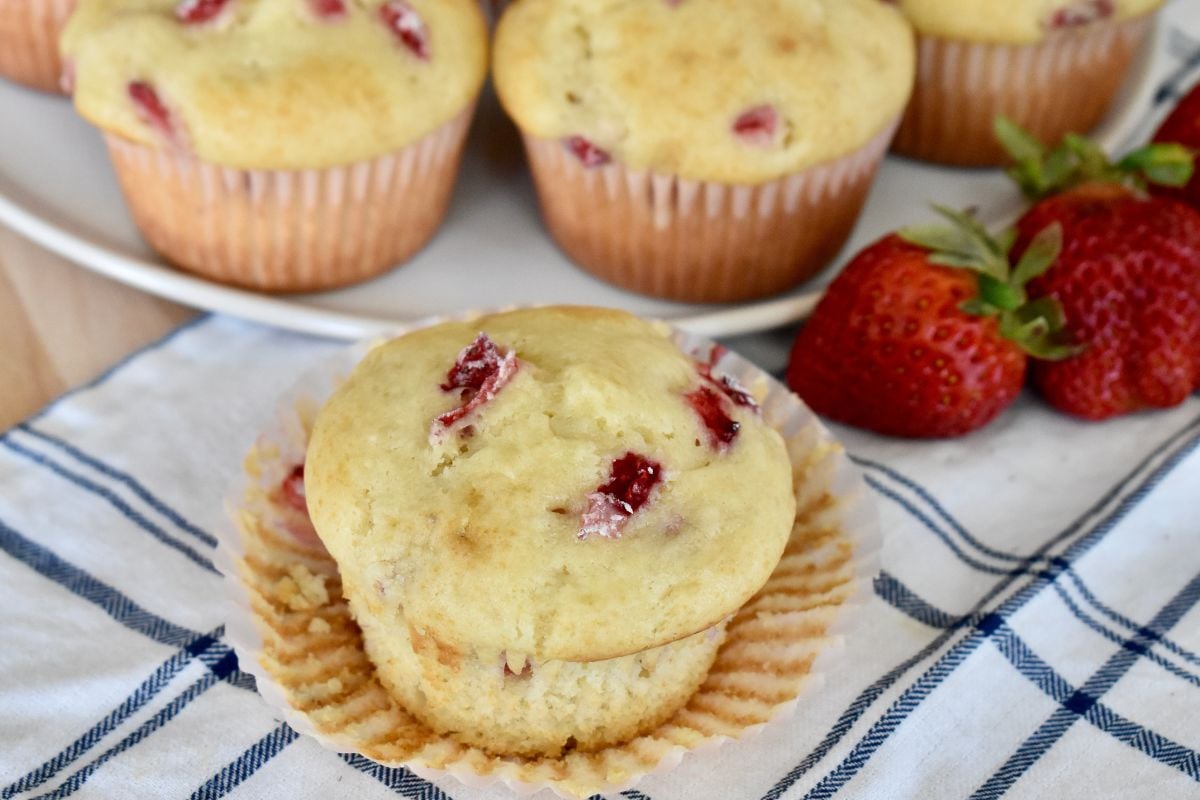 Strawberry Cream Cheese Muffins on a white dish towel with fresh strawberries. 