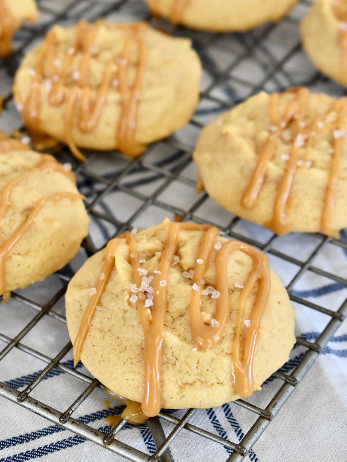 Dulce de leche cookies with dulce de leche drizzle on top and sea salt on a cooling rack. 