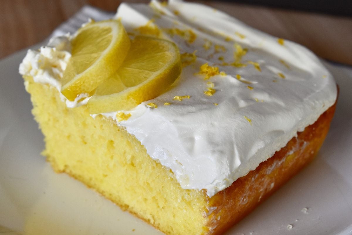 Slice of lemon poke cake made with lemon cake mix and lemon gelatin with a whipped topping on a white plate. 