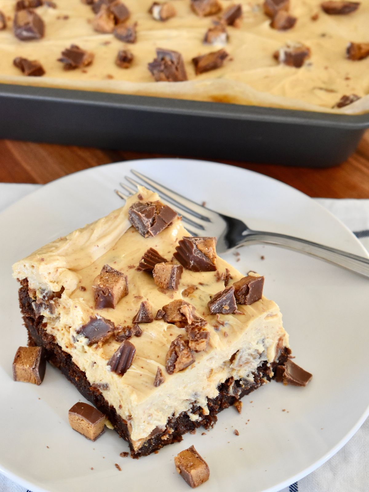 Peanut Butter Cheesecake Brownies on a plate with Reese's Peanut butter cups sprinkled on top. 