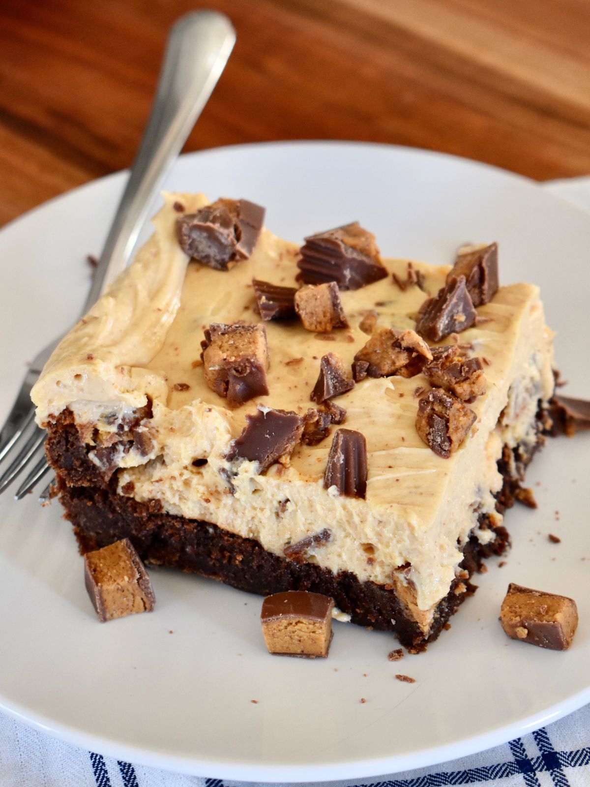 Peanut Butter Cheesecake Brownie slice on a white plate with a fork. 