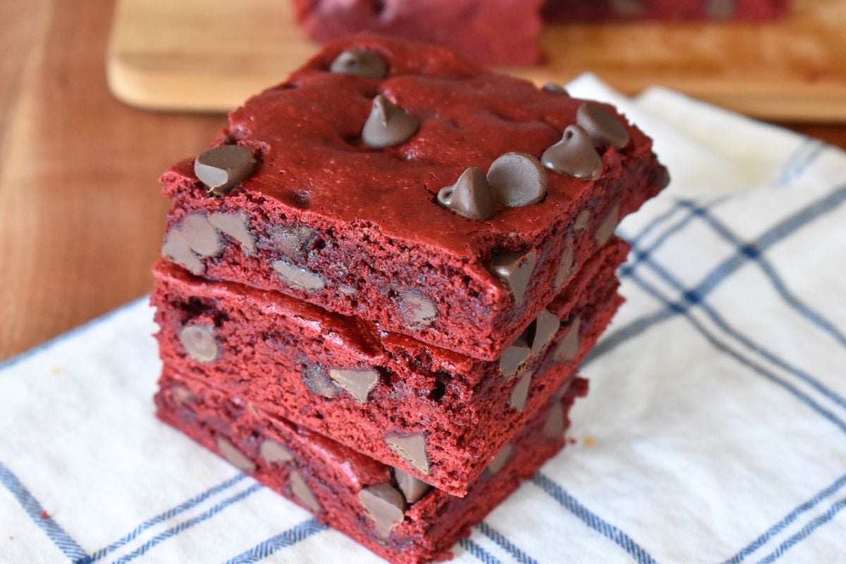 Red velvet cake mix brownies with chocolate chips stacked on each other on a white napkin. 