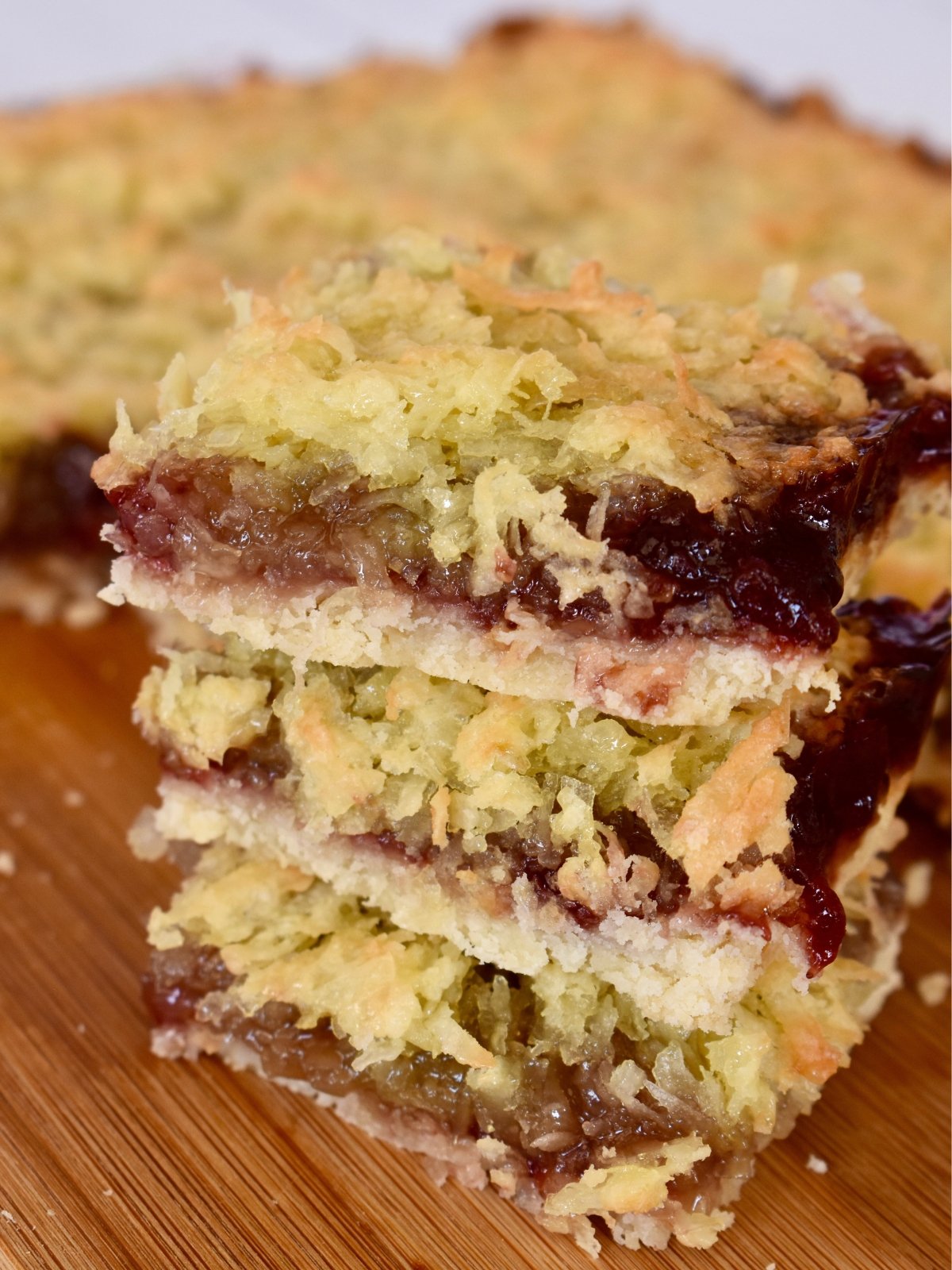 Raspberry Coconut Bars stacked on a wood cutting board.